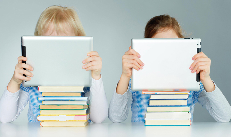 Two pupils leaning on a pile of books while reading on touchpad